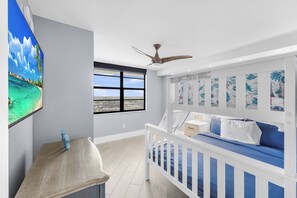 A room with a bunk bed, a ceiling fan, a large window, and a wall-mounted TV.