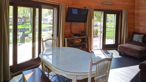 A wooden cabin interior with a dining table, chairs, a television, and a couch.