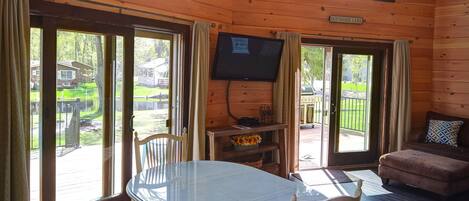 Een houten hut van binnen met een eettafel, stoelen, een televisie en een bank.