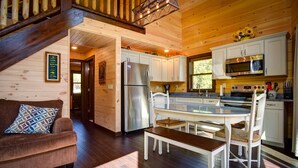A wooden cabin interior with a kitchen, dining area, and a staircase.
