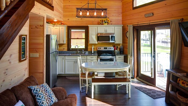A cozy cabin interior with a wooden staircase, a dining area, and a kitchen.