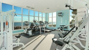 Une salle de sport équipée de machines de cardio, de poids libres et offrant une vue sur la plage.