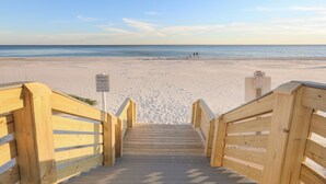 Un escalier en bois mène à une plage où se trouve un panneau indiquant un système d’alerte par drapeaux.