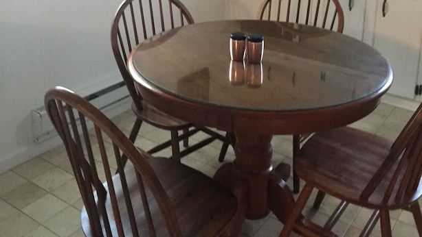 Een eetgedeelte met een ronde tafel, vier houten stoelen, een zwarte magnetron en witte kasten.