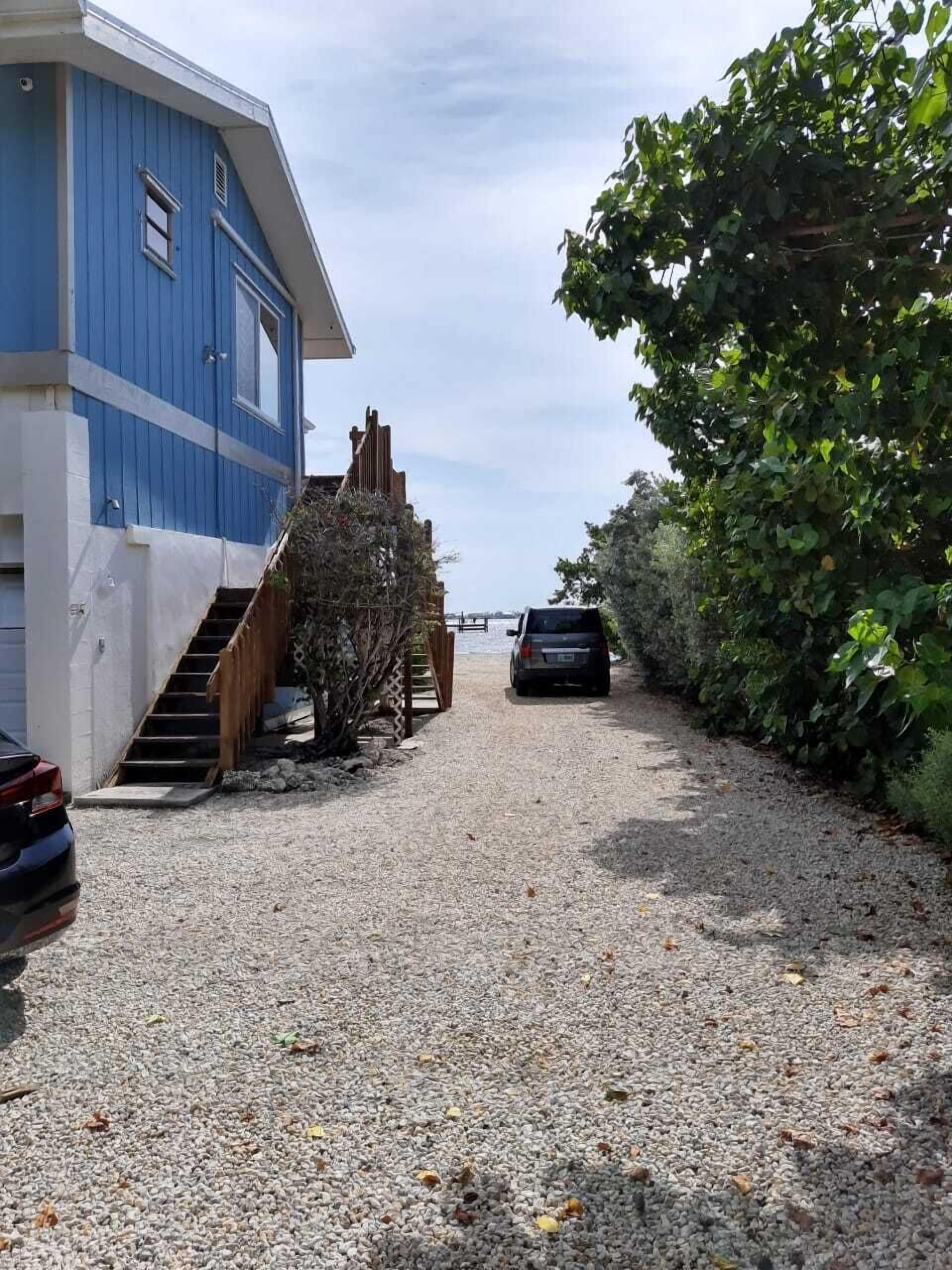 A gravel driveway leading to a blue building with a staircase.