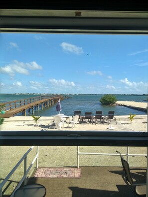 A beachside view with a wooden pier extending into the water, a sandy area with lounge chairs and umbrellas, and a clear blue sky. - OCEAN FRONT PARADISE/290 ft PRIVATE DOCK/AWESOME VIEWS (Little Torch Key)