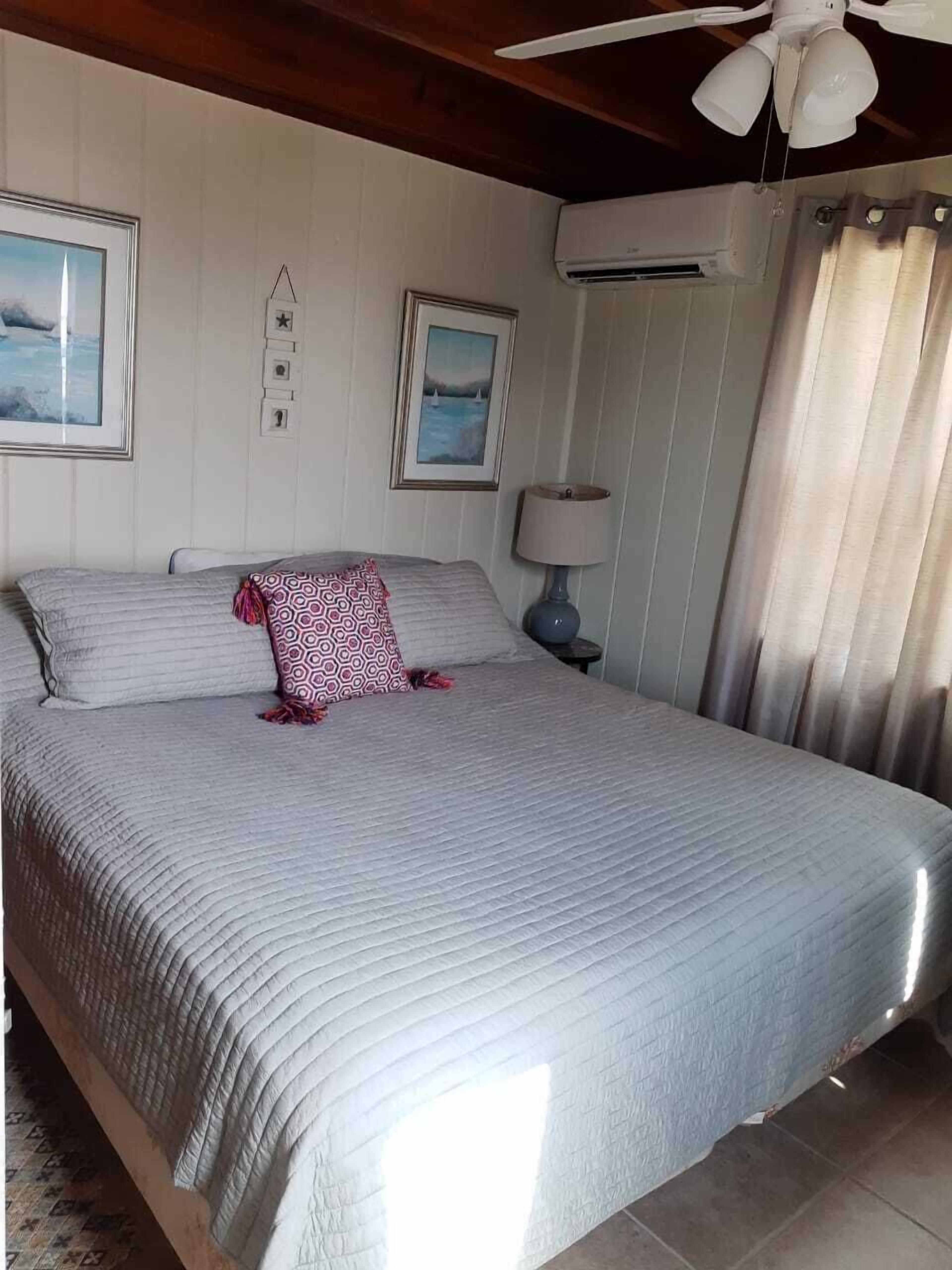 Ein Schlafzimmer mit einem großen Bett, einem Deckenventilator, einer Klimaanlage und zwei gerahmten Bildern an der Wand.