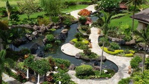 Un jardín ajardinado con un estanque, senderos de piedra y plantas tropicales.
