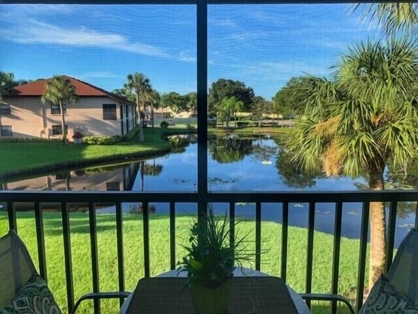 A view from a balcony with a water feature, a lawn, and a building with a red roof.
