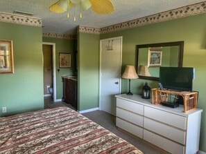 A bedroom with a bed, dresser, television, and a door leading to another room.