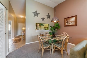 A dining area with a glass table, wicker chairs, and a hanging pendant light. - Shorewalk 202/4625 - Bradenton-Condo 2 Bedroom/ 2 Bath, 5 miles from Anna Maria Island and near Img, maximum occupancy of 4 people. (Bradenton)