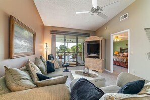 A spacious living room with a sofa, a television, and a ceiling fan. There is a balcony with a view of the outdoors. - Shorewalk 202/4625 - Bradenton-Condo 2 Bedroom/ 2 Bath, 5 miles from Anna Maria Island and near Img, maximum occupancy of 4 people. (Bradenton)