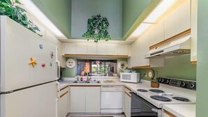 Una cocina compacta con armarios blancos, un microondas, una estufa y un fregadero.