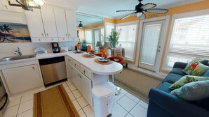 A modern kitchen with white cabinets, a dishwasher, and a central island with decorative plates. - Sunny Poolside Retreat | Bright & Stylish Condo with Resort Amenities! (Galveston)
