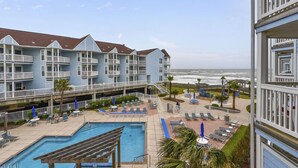 A beachfront hotel with a pool, lounge chairs, and a view of the ocean. - Sunny Poolside Retreat | Bright & Stylish Condo with Resort Amenities! (Galveston)