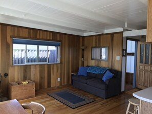 A living room with a dark sofa, wooden walls, a large window, and a small table. - Crows Nest, on the Bluff over Trinidad Bay, amazing views! (Trinidad)