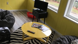 Un salón con una mesa de centro amarilla, un sofá de cuero negro y una alfombra estampada de cebra.