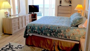 A bedroom with a bed, dresser, TV, and a balcony view.