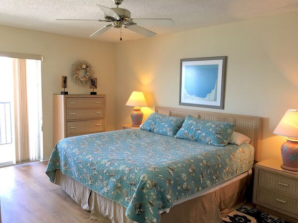 A bedroom with a bed, two bedside tables, a ceiling fan, a dresser, and a wall-mounted picture.