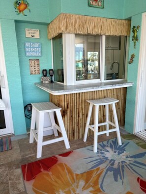 A bar area with two stools, a counter, and a sign that reads 'NO SHIRT NO SHOES NO PROBLEM'.