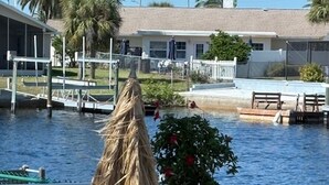 A waterfront patio with a thatched umbrella, a potted plant, and outdoor seating. -  The Crab Shack,Paradise on the Gulf includes pontoon boat  and salt water pool. (New Port Richey)