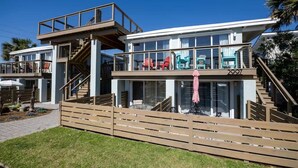A modern multi-story building with a glass facade, outdoor seating area, and a wooden deck. - Wanna Sea #202 - Newly Renovated Balcony! (Fernandina Beach)