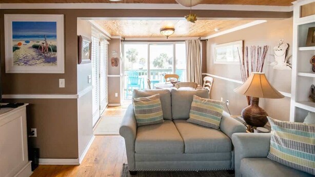 A living room with a sofa, a ceiling fan, a lamp, and a painting on the wall. - Wanna Sea #202 - Newly Renovated Balcony! (Fernandina Beach)