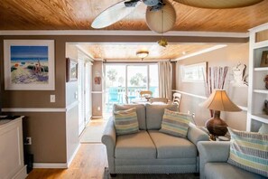 A living room with a sofa, a ceiling fan, a lamp, and a painting on the wall.
