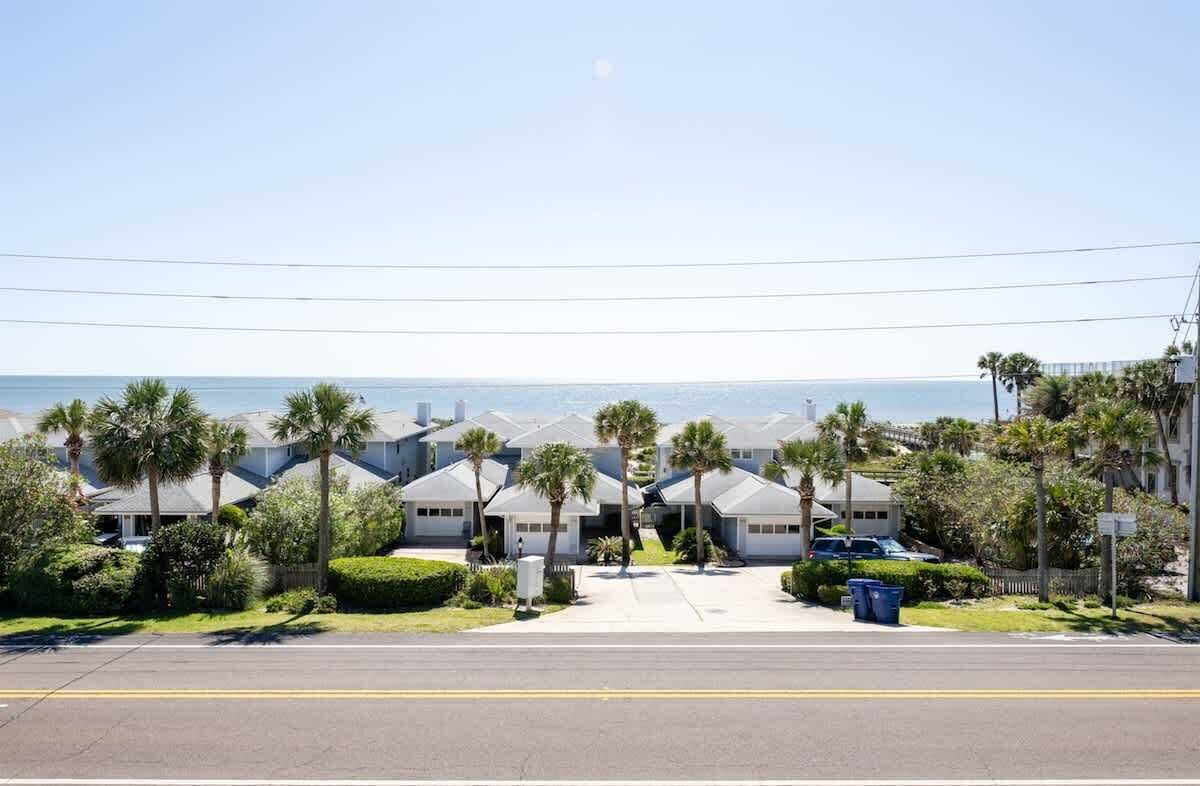 A residential street with houses, palm trees, and a clear view of the ocean.