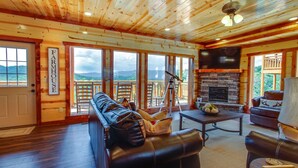 A cozy cabin interior with a fireplace, leather seating, and a balcony with a scenic mountain view. - A Heavenly View ~ 6 BR Indoor Pool Cabin ~ Sleeps 28 ~ Incredible Views! (Sevierville)