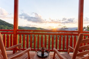 A wooden deck with a table set for two, overlooking a mountainous landscape during sunset. - A Heavenly View ~ 6 BR Indoor Pool Cabin ~ Sleeps 28 ~ Incredible Views! (Sevierville)