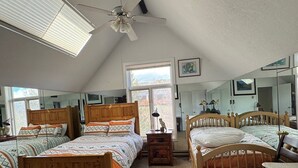Une chambre avec trois lits en bois, un ventilateur de plafond, une lucarne et de grandes fenêtres.