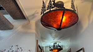 Un couloir avec une porte en bois, un luminaire mural orné d’une silhouette de cerf et d’arbre, et une branche parsemée de baies rouges.