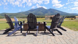 Four Adirondack chairs arranged around a table on a paved patio with a mountain view in the background. - Modern Mountain Getaway (Flagstaff)