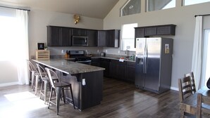 A modern kitchen with dark cabinets, stainless steel appliances, and a large island with bar stools. - Modern Mountain Getaway (Flagstaff)