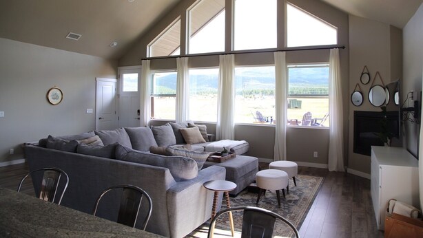 A spacious living room with a large gray sectional sofa, a small round table, and a flat-screen TV mounted on the wall. - Modern Mountain Getaway (Flagstaff)