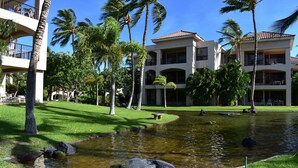 A hotel with a courtyard featuring a pond, palm trees, and a well-maintained lawn.