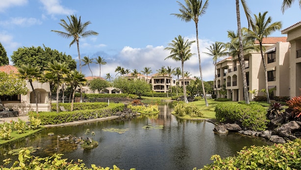 Un resort con un estanque central, palmeras y un edificio con varios balcones.
