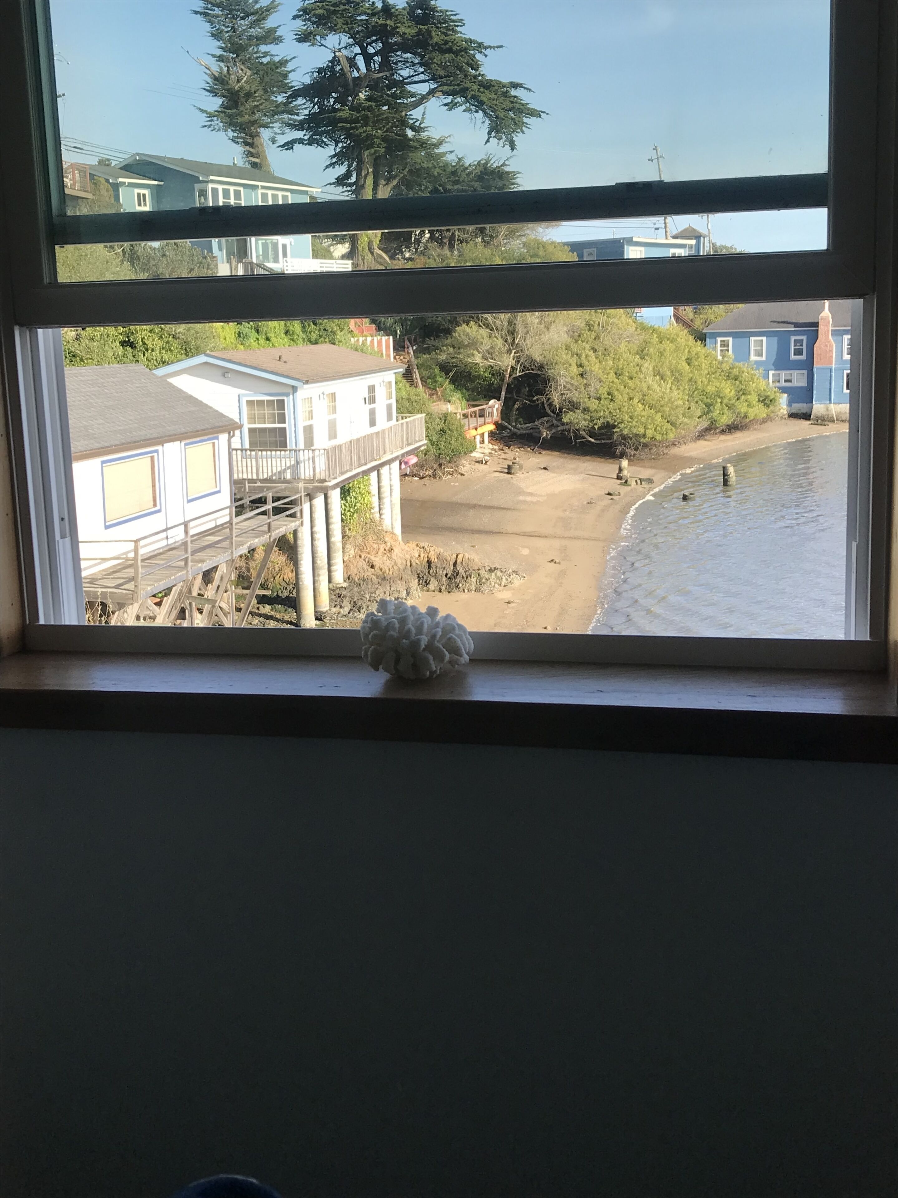 A view through a window of a beach with a wooden deck, a sandy shore, and a blue building in the background.