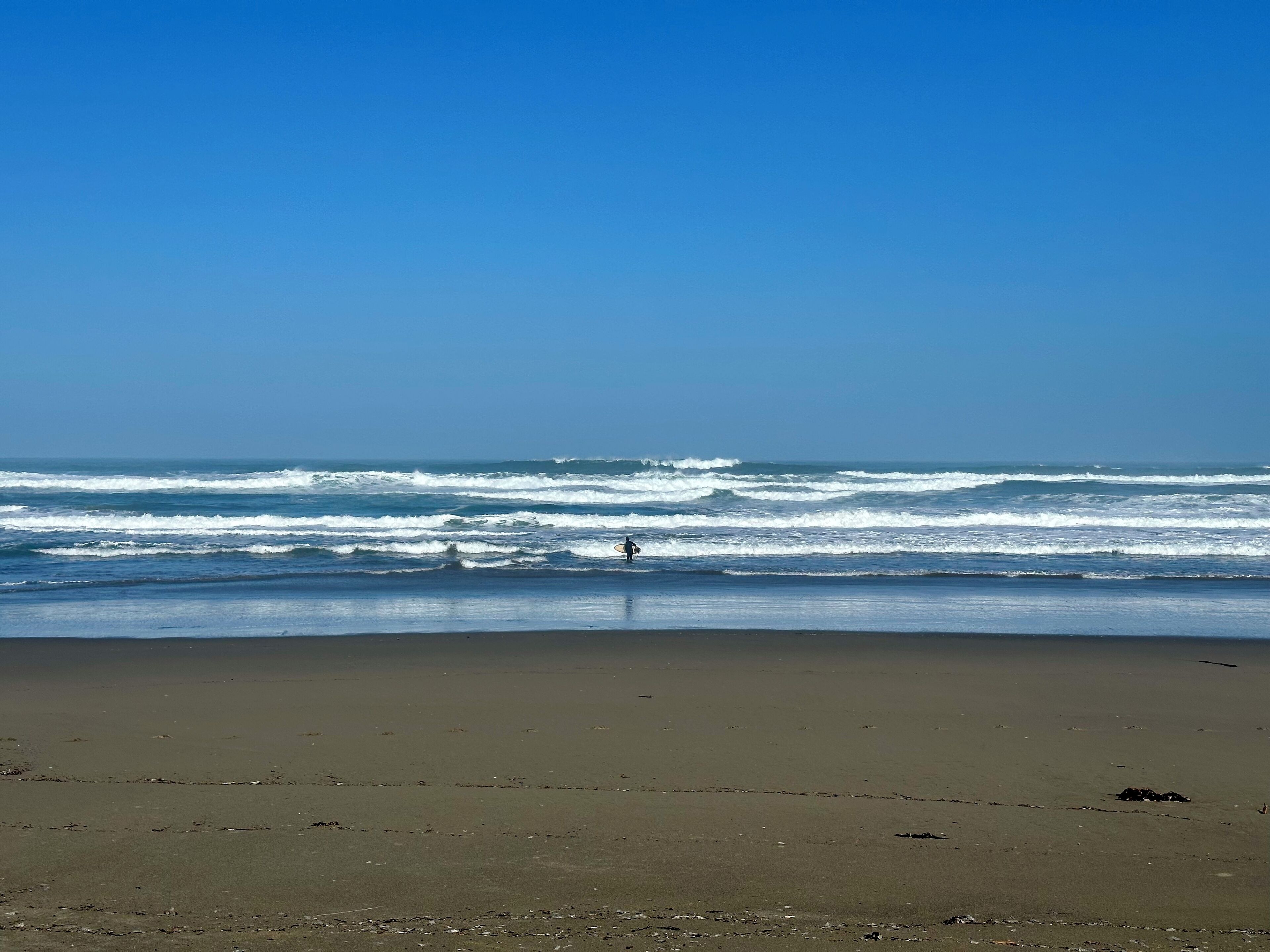 A beach with waves and a person in the water.
