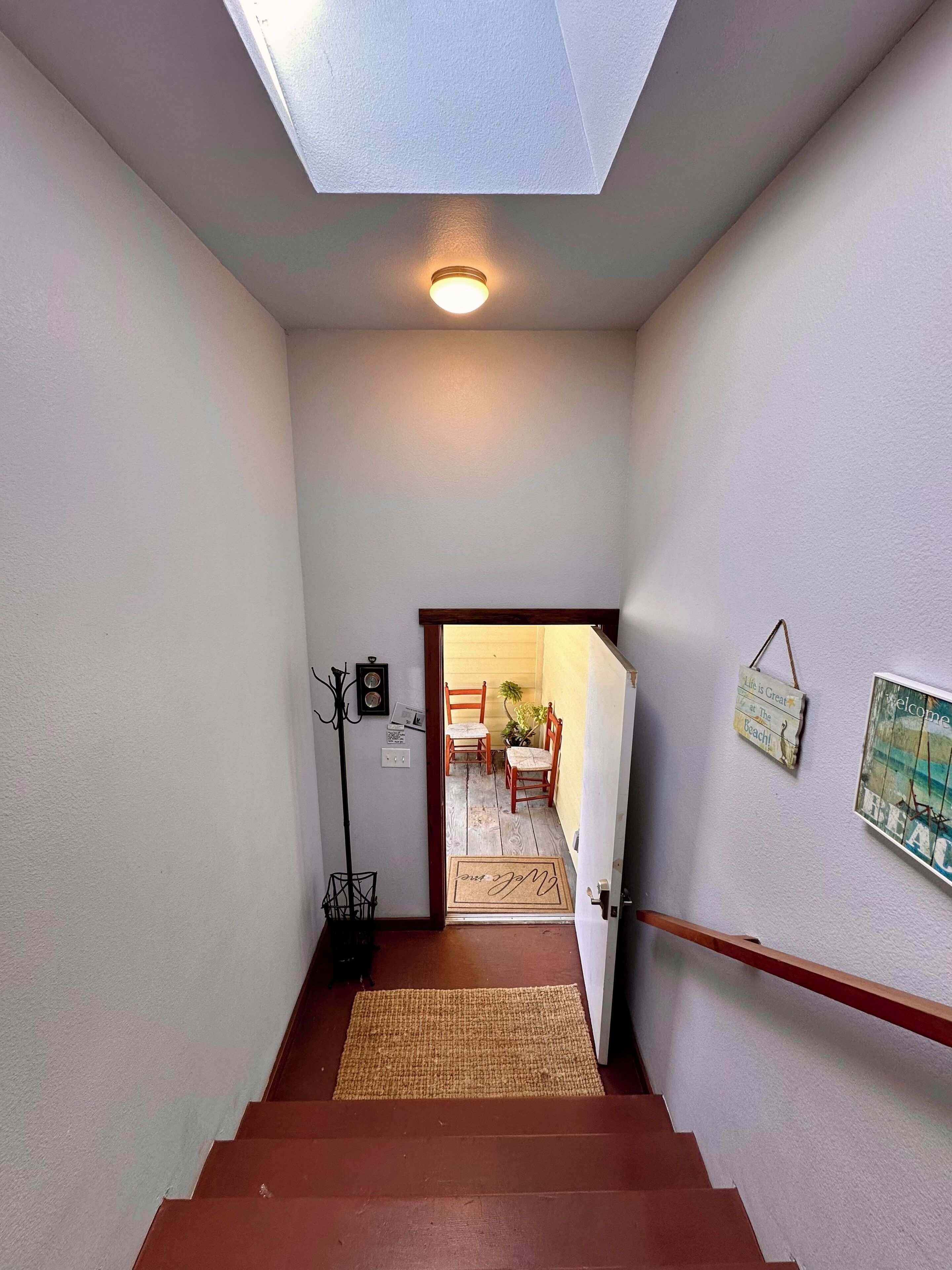 En trappe fører op til et rum med ovenlys, en træstol, et lille bord og en dør med dørmåtte.