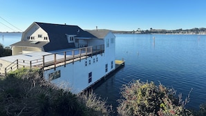Una casa flotante blanca amarrada en un muelle, con vista clara al agua y a la costa distante.