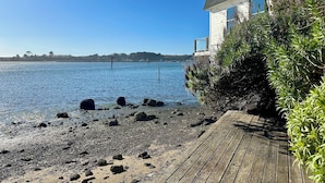 Una terraza de madera que da a una costa rocosa, con una casa a la derecha.