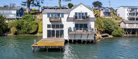 Una casa flotante con balcón, terraza y un pequeño muelle que se adentra en el agua.