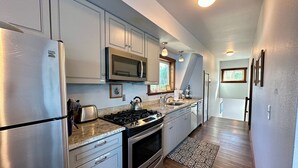 Una cocina moderna con electrodomésticos de acero inoxidable, estufa a gas y microondas. Hay una ventana que proporciona luz natural y una alfombra estampada en el suelo.