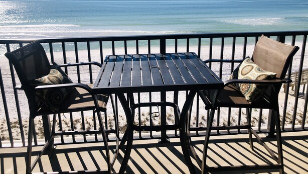 A deck with a table and two chairs facing a beach with ocean views.