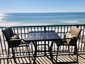 Une terrasse avec une table et deux chaises, donnant sur une plage et l’océan.