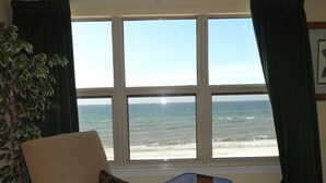 A room with a large window overlooking the ocean, a chair with a patterned pillow, and a small table.