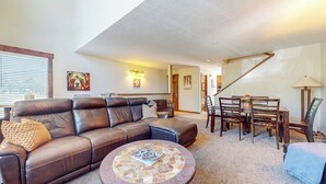 Ein Wohnzimmer mit braunem Ledersofa, einem runden Couchtisch und einem Essbereich mit Holztischen und -stühlen.