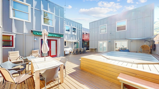 Eine Terrasse mit Gartenmöbeln, einem Whirlpool und einem Gebäude mit mehreren Fenstern und Türen.